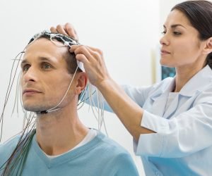 Carefully and gently. Pleasant young female doctor fixing electrodes on the head of her patient while preparing him for the electroencephalography procedure